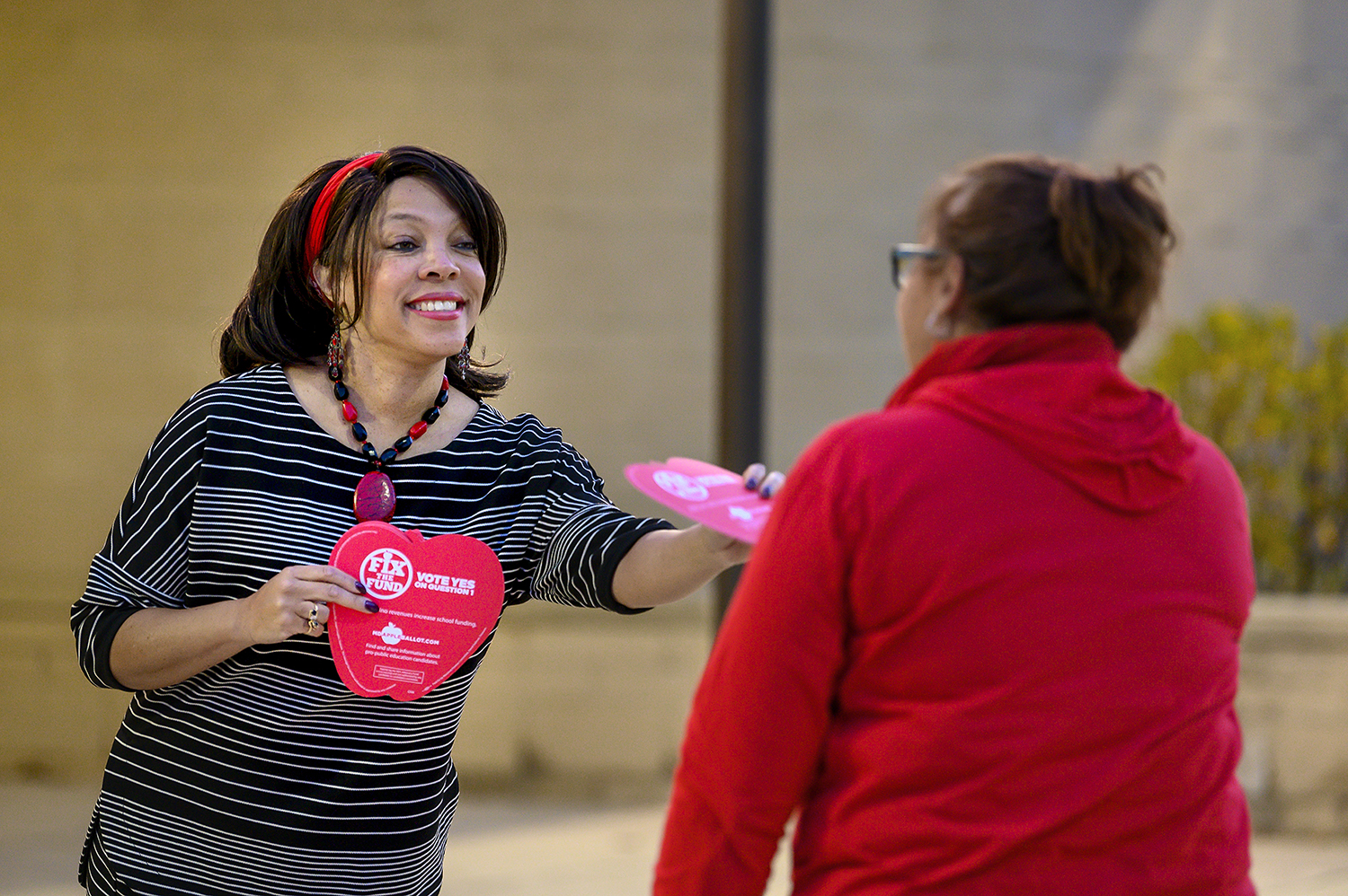 Woman handing apple-shaped sample ballot to person